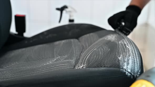 Working cleaner at car wash. Cleaning a seat using a brush and chemical solution. Slow motion