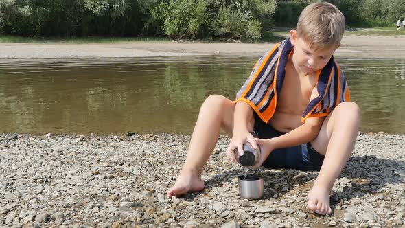 Boy Teenager Schoolboy with a Naked Body with a Towel Around His Neck Sits on the Banks of the River