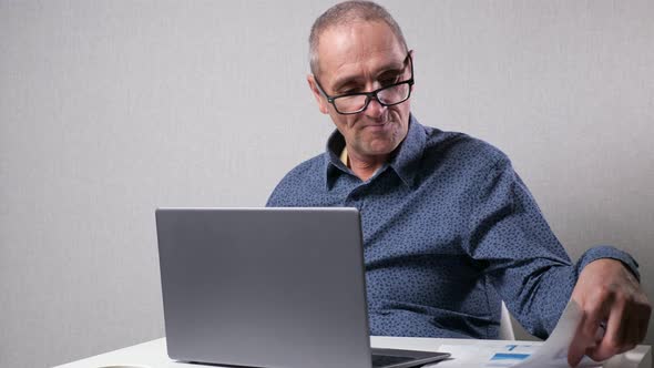 Senior Man Sits Near Computer Checking Reports in Office