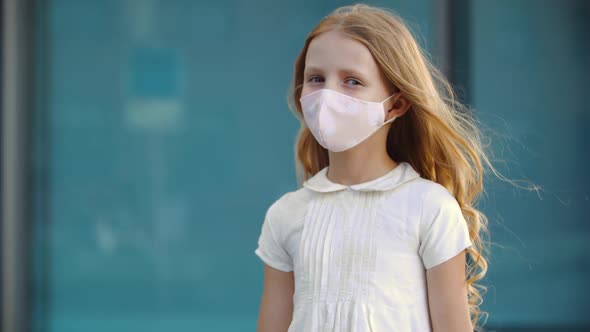 Serious Young Girl with Long Golden Blonde Curls Wears White Dress and Pink Protective Face Mask