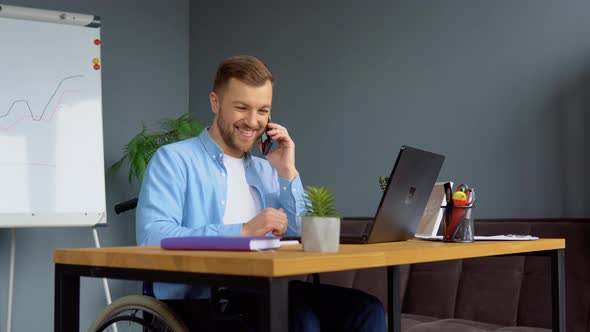 Motivated Cheerful Handicapped Freelancer Talking on the Phone and Taking Notes Sitting in