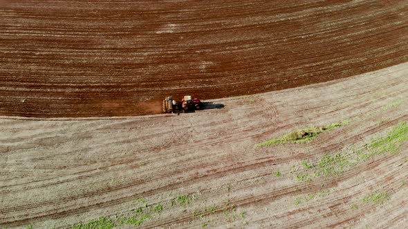 Aerial view shot of a farmer in tractor seeding, sowing agricultural crops at field