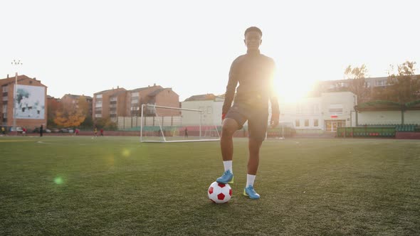 A Pleasant Young Black Girl Stands in a City Stadium and Puts Her Foot on a Soccer Ball Against the