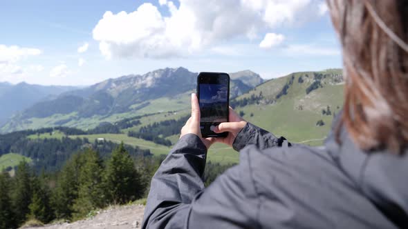 Young girl taking panorama photos of beautiful mountain landscape in Switzerland during sunny and wi