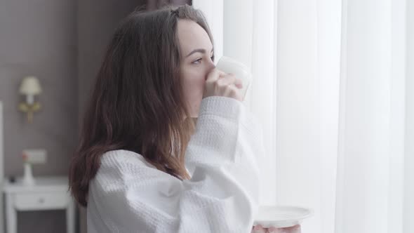 Side View of Brunette Caucasian Woman Drinking Coffee in the Morning in Hotel Room. Close-up