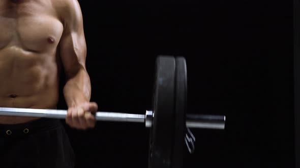 Man is Doing Exercises with a Barbell Training on a Black Background in the Studio