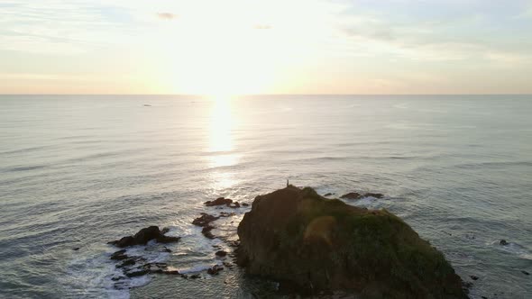 4k drone slowly approaching then flying over a giant beach rock during majestic sunset. One man stan