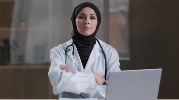 Happy Smiling Arabian Nurse Islamic Doctor Therapist Wear White Uniform Coat Hijab Sitting at Clinic
