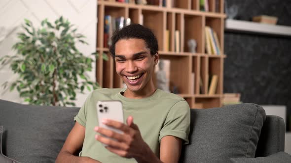 Hilarious Darkhaired Man in Casual Wear Using Smartphone for Virtual Meeting