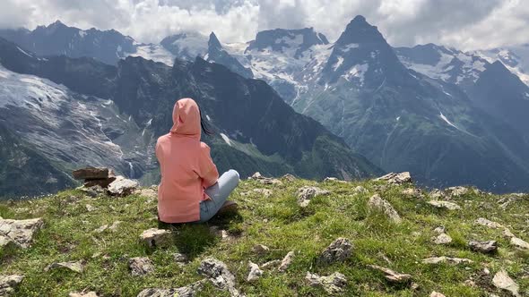 Young Woman Sitting on Rock and Looking at Mountain Landscape