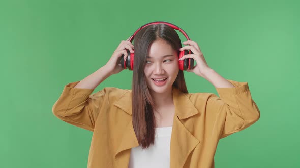 Asian Woman Listening To Music With Headphones And Dancing In The Green Screen Studio