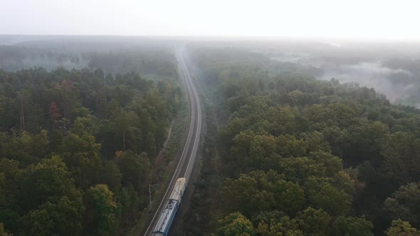 Railroad in a beautiful foggy forest with a passing city train early in the morning.