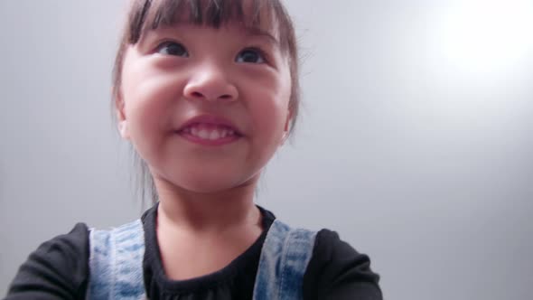 Happy little asian girl using smartphone for video call, waving hand and speaking and talking witn s