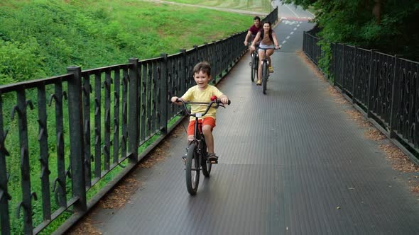 Happy family crossing metal bridge on bikes