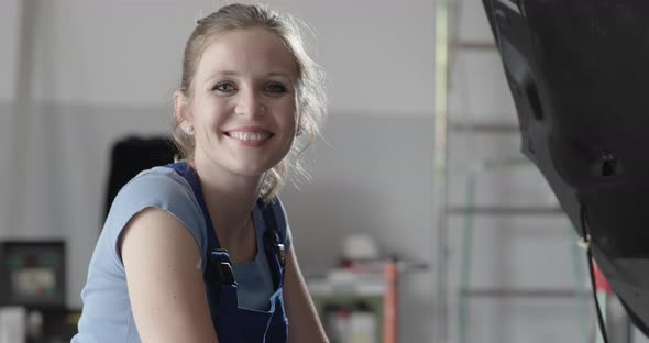 Female mechanic working in the car shop, she is smiling at camera