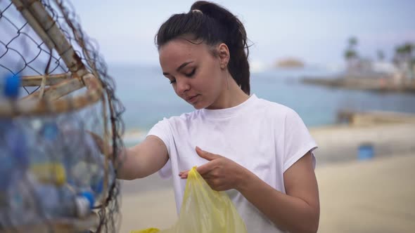 Beautiful Young Slim Caucasian Woman Putting Empty Plastic Bottles in Special Place on Coast Beach