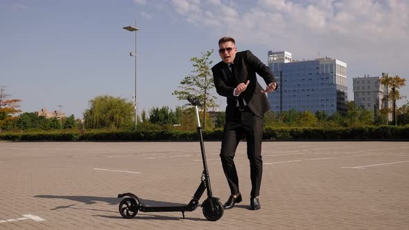 Successful Businessman Is Dancing in a City Park, Next To an Electric Scooter.