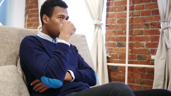 Young African Man Drinking Coffee From Cup Sitting on Sofa