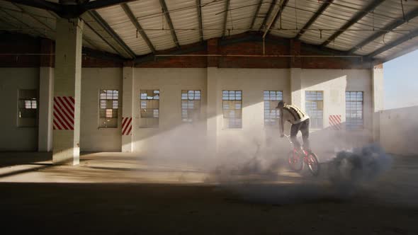 BMX rider in an empty warehouse using smoke grenade