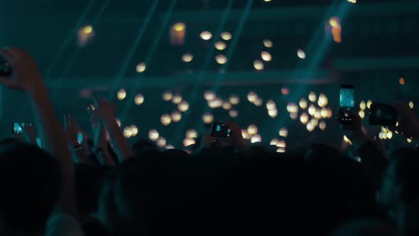 Music fans in concert hall waving lights and shooting with cellphones