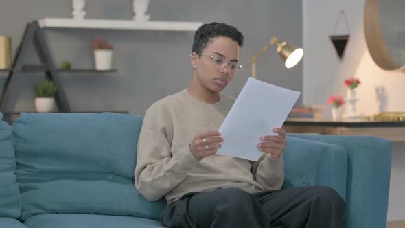 African Woman Reacting to Loss on Documents Sofa