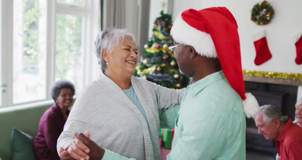 Happy diverse senior couple dancing together with friends in background at christmas time