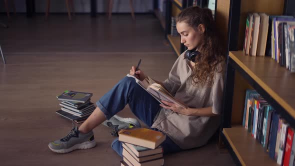 Student in Headphones Sitting Against Bookshelf with a Books on the Floor