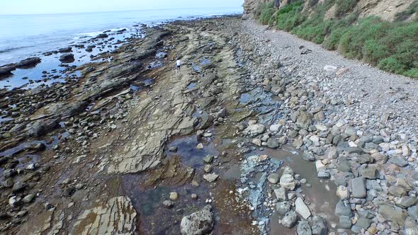 Tracking shot of a young man running on a rocky ocean beach shoreline