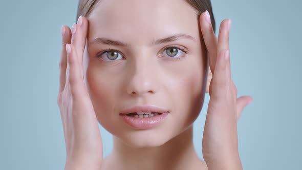 Headshot of Millennial Woman Touching Face with Both Hands While Looking to Camera and Smiling 