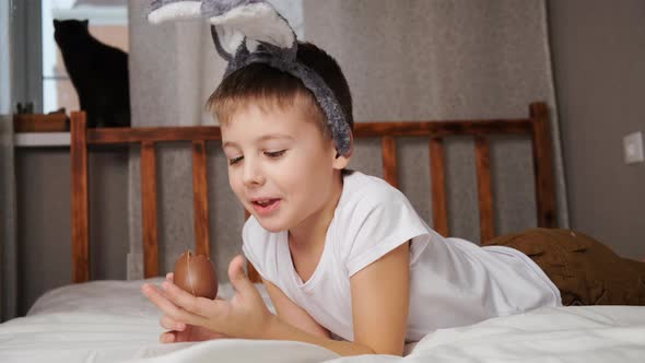 Little Boy with Bunny Ears Eating Easter Chocolate Egg