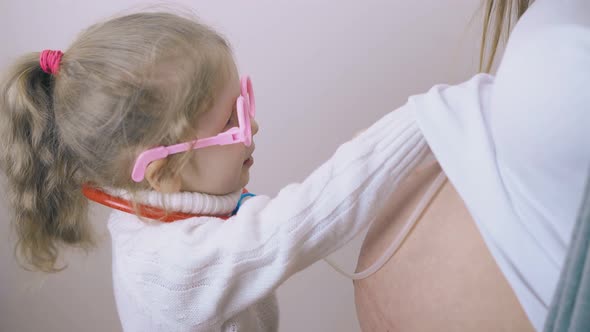 Little Girl in Funny Glasses Plays Doctor with Pregnant Mom