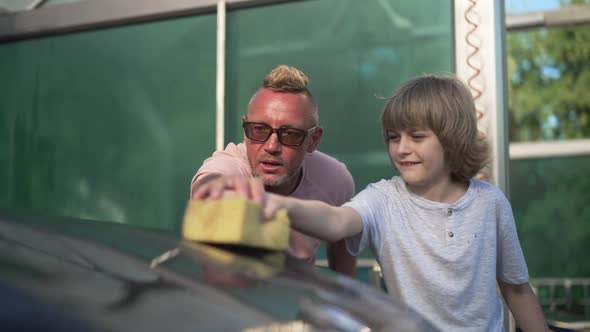 Happy Son Helping Father Washing Car Hood with Sponge in Slow Motion Outdoors