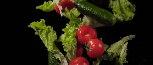 Tasty Tomatoes Cucumbers and Lettuce Fly Around on a Black Background in Slow Motion Shot Water