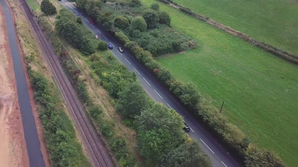 Aerial tracking along a busy english country main road, surrounded by trees, fields and a railway tr