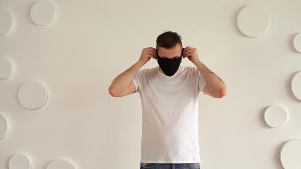 Handsome Young Man in Black Medical Mask Posing on Background of White Wall