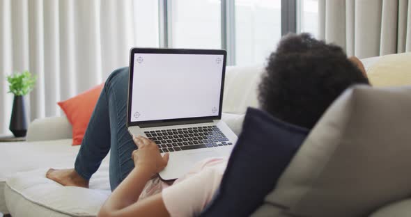 Happy african american woman sitting on sofa, using laptop with copy space