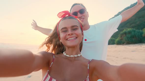 Happy Young Caucasian Man Hugs Woman From Behind to Take Selfie on Sea Coast