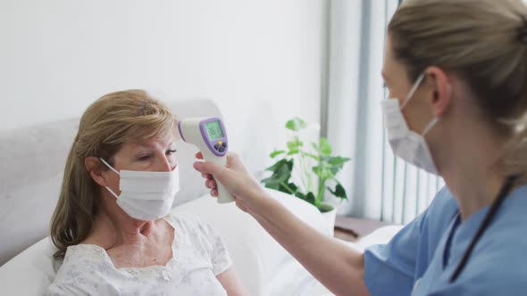 Female health worker checking temperature of senior woman at home