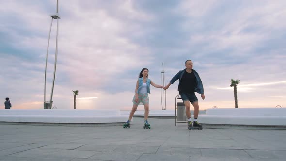 Beautiful Sweet Couple Riding on Roller Skates Quads Holding Hands Near the Sea Slow Motion