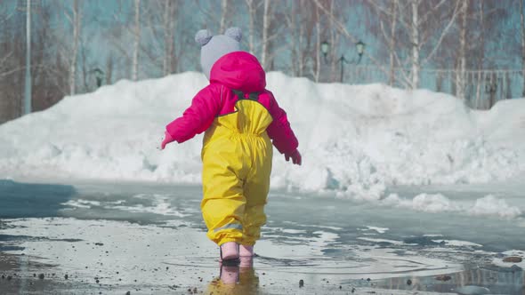 Toddler walk through puddles in the spring in a yellow rubber jumpsuit.