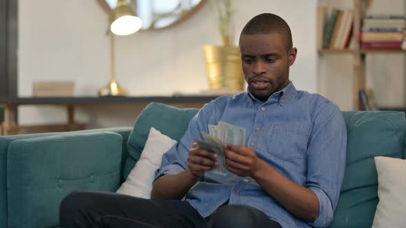 Successful Young African Man Counting Dollar on Sofa