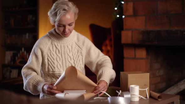 Happy Young Woman Wrapping Festive Christmas Gift Box in Craft Paper with Presents for Family