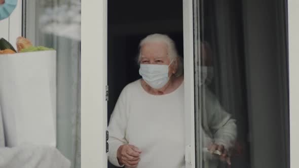 Young Woman In Medical Mask Brought Food To An Elderly Woman During Quarantine