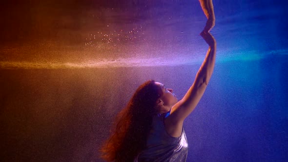 Woman Is Floating Inside Pool Underwater and Stretching Hand To Surface, Touching Reflection