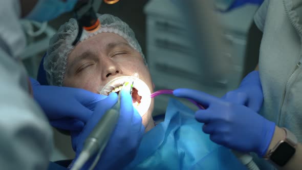 Closeup Portrait of Caucasian Patient in Dental Chair Closing Eyes As Doctor Drilling Ill Tooth and