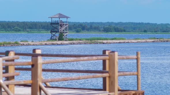 View of footbridge path and birdwatching tower at lake Liepaja in sunny summer day with scenic cumul