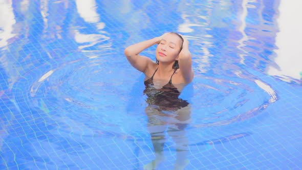 High angle. An attractive young woman in a swimming pool smooths back her wet hair then looks around