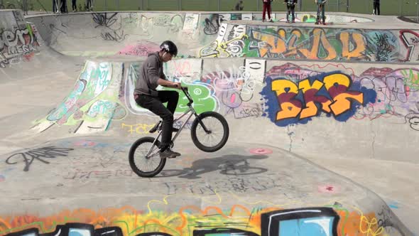 A young man rides a BMX bicycle in a concrete skate park.