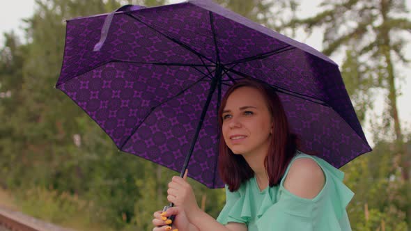 Young Woman with Umbrella Sits on Railway in Cloudy and Windy Weather