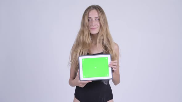 Happy Young Blonde Woman in Swimsuit Thinking While Showing Digital Tablet